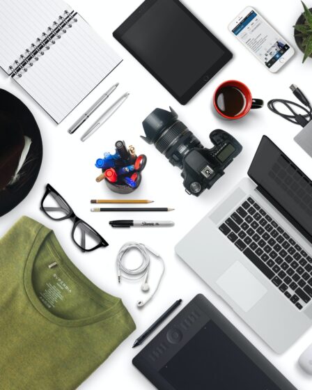 Diversos produtos espalhados sobre um local branco: Camisa, óculos, câmera, Notebook, papelaria